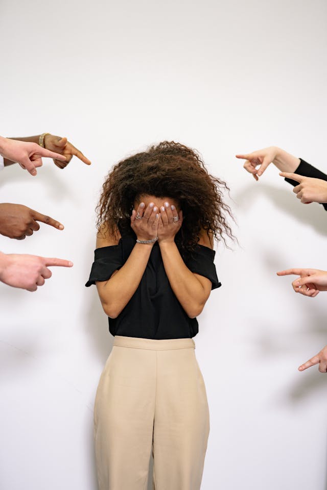 Woman covering her eyes while others point at her, representing anxiety and social pressure